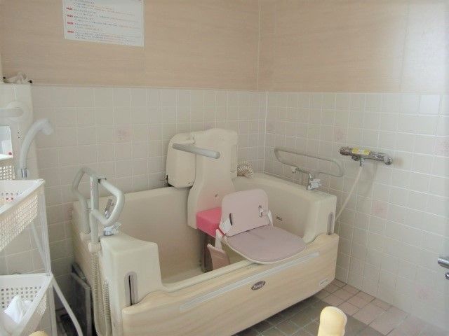 ピンクと白のタイルが貼られた明るい浴室。座ったまま入浴できる機械浴が置かれている。