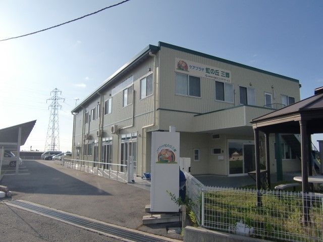 ２階建てのベージュを基調とした建物。玄関には大きな屋根が付いている。