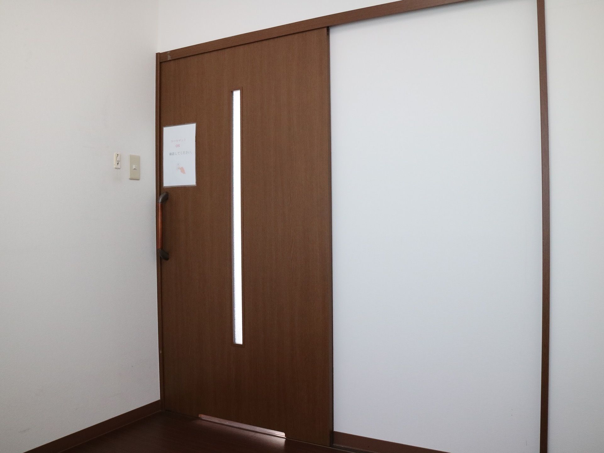 白色の壁、濃い茶色の建具にデザインされた居室である。扉の中央に縦長の明かり窓が設置されている。引き戸式仕様。