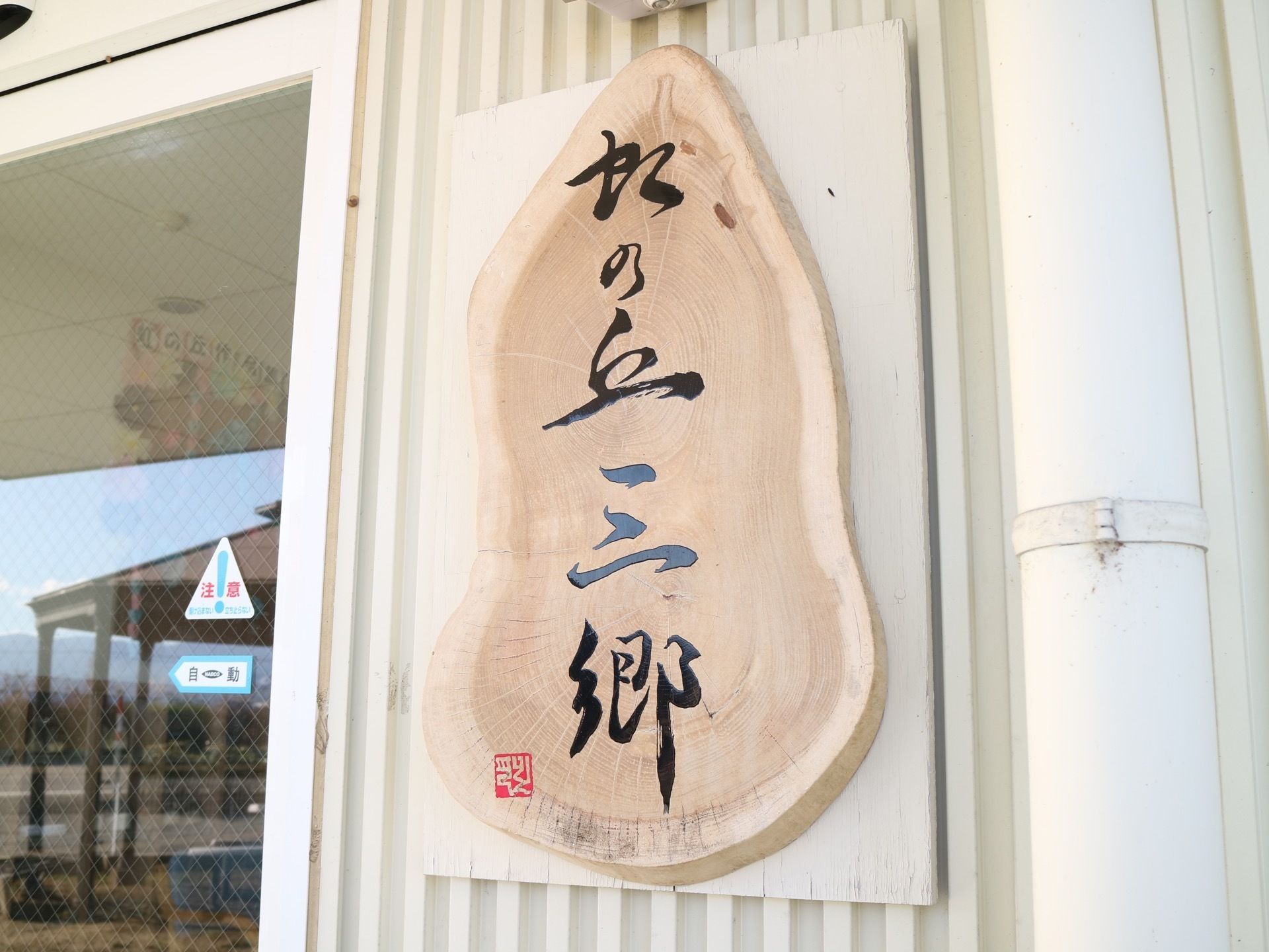 自動ドアのとなりに、木材を仕様した看板が設置されている。黒文字で施設名が書かれている。左下に角印もある。