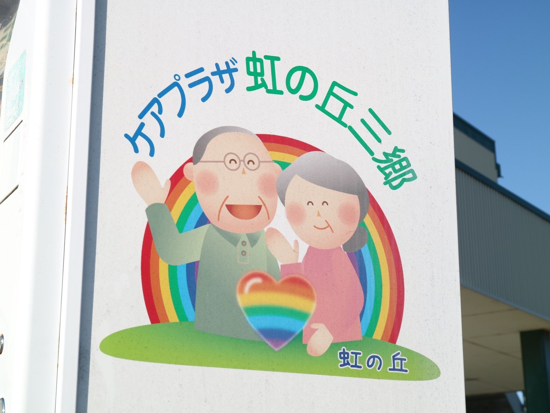 真っ白な壁に入居者様をイメージした、イラストが描かれている。ブルーとグリーンで施設名が記されている。