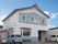 白とブルーの外壁で三角屋根が付いている2階建ての建物は玄関に屋根があり、敷地内に駐車場があり、アットホームな雰囲気。