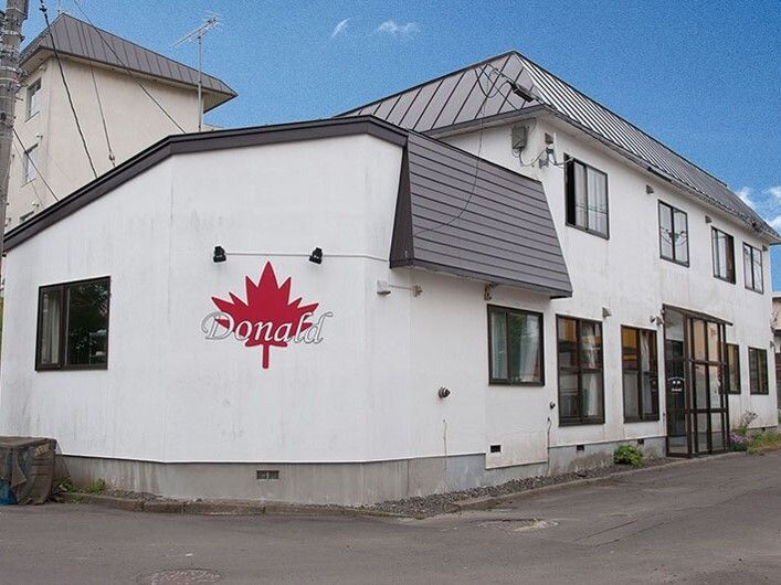 赤いメープルの歯のイラストの上にはCanadaと書かれ、グレーの屋根が付いた２階建ての建物。