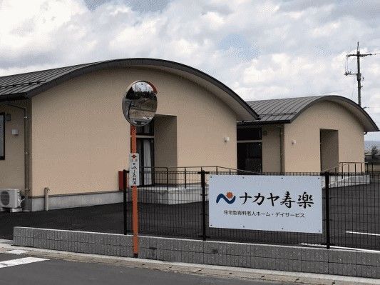 平屋建ての建物が二つ並び、広い駐車場がある。敷地内を囲むフェンスにはホームの看板が設置されている。