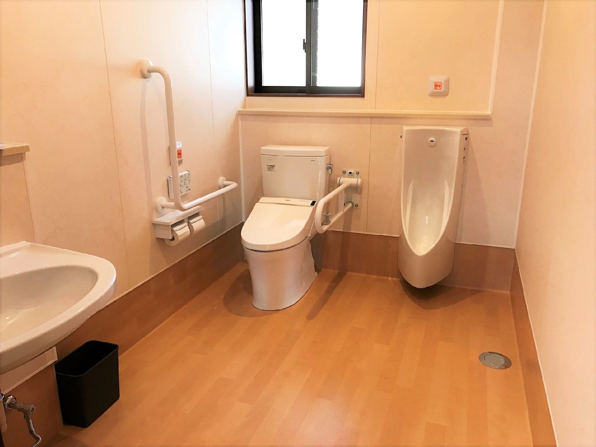 広いトイレにはエル字型の壁に設置された手すりや手洗い場、男性用トイレがある。