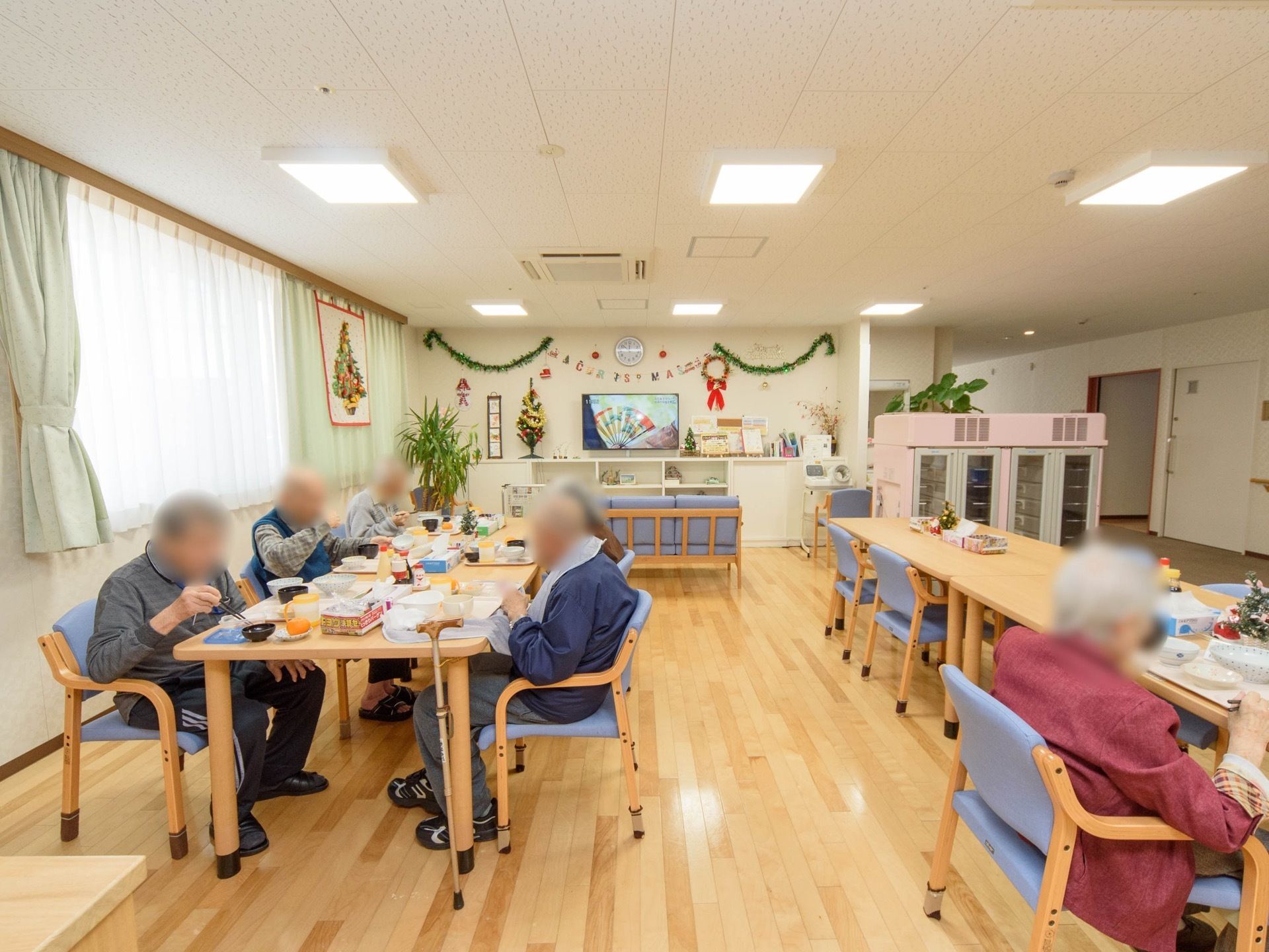 食堂で大勢の入居者様が食事をしている。壁面には季節感のある装飾がされている。食卓にも季節の置き物が置いてある。