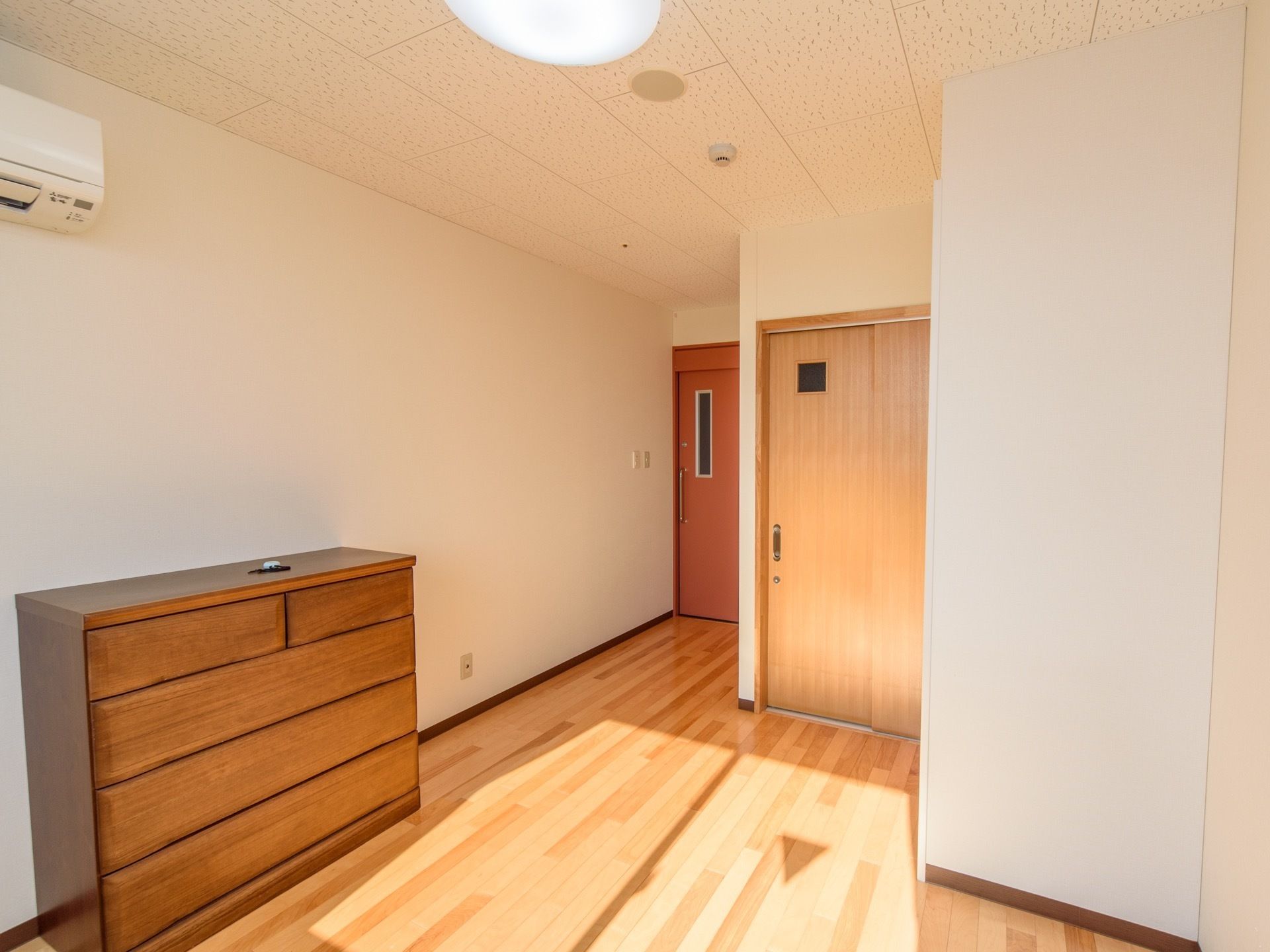 白い壁紙とフローリング、家具や建具にも木を使用した温かみのある明るい居室。右の大きな扉の奥は広いトイレがある。