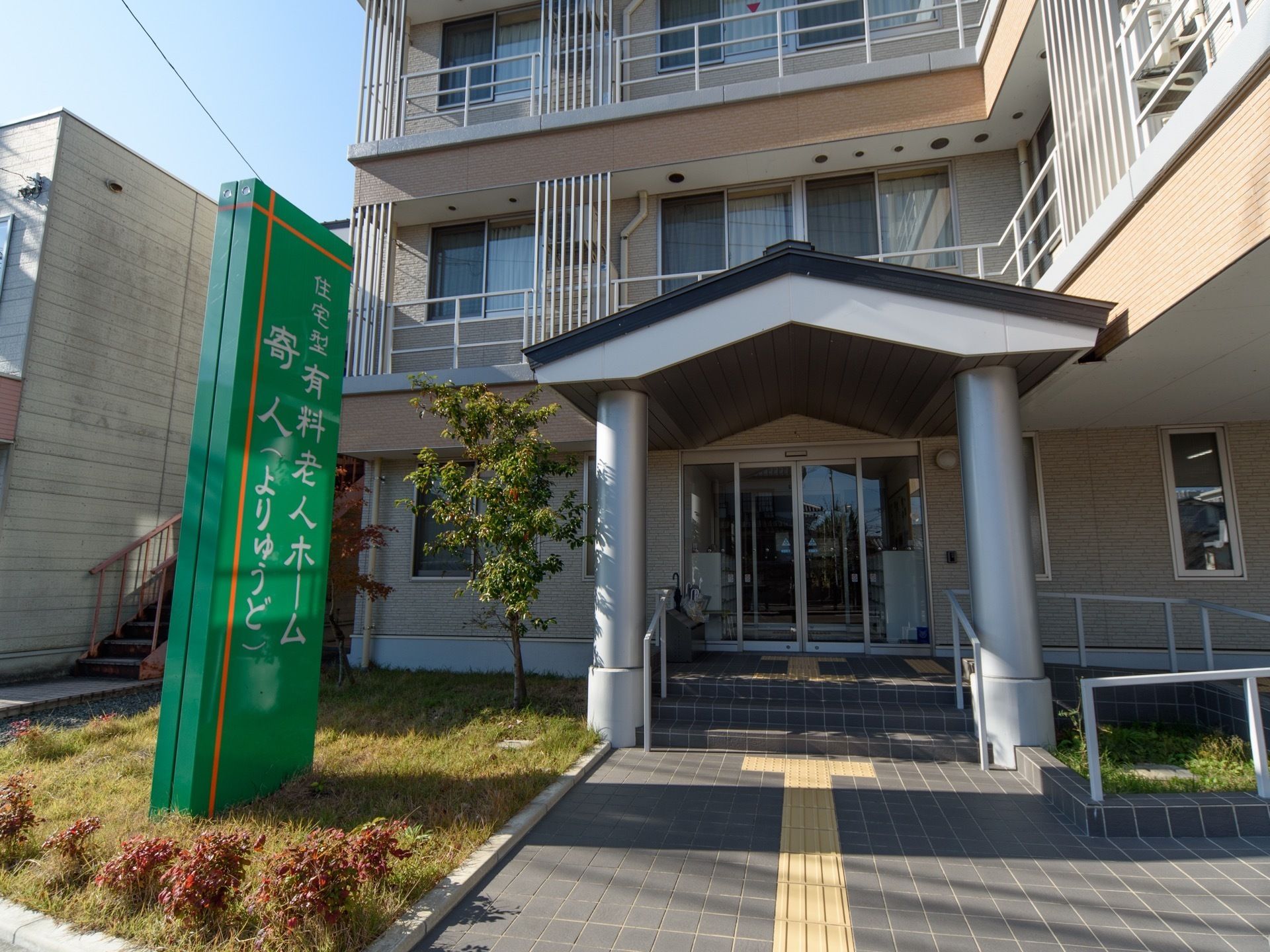 建物のエントランス部分には、アプローチの両側に植栽があり、格調高い。道路寄りに目を引く緑色の大きな看板がある。