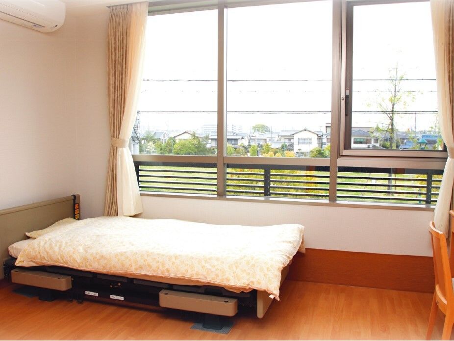 シンプルな居室にはエアコンがあり、大きな窓にはカーテンがあり、寝具付きのベッドがついている。