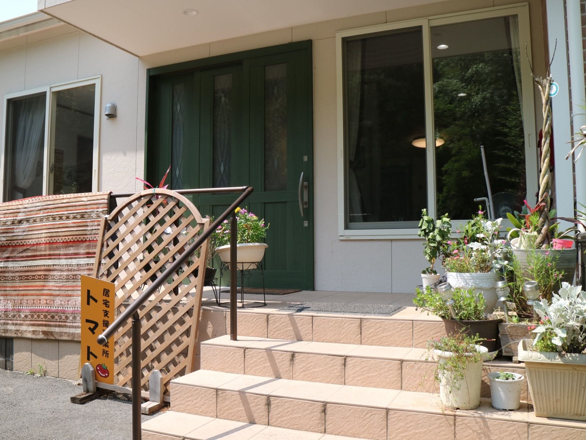 緑色のスライド式の扉の両側には窓がある。扉の前には手すり付きの階段があり、階段の右側には植物が置かれている。