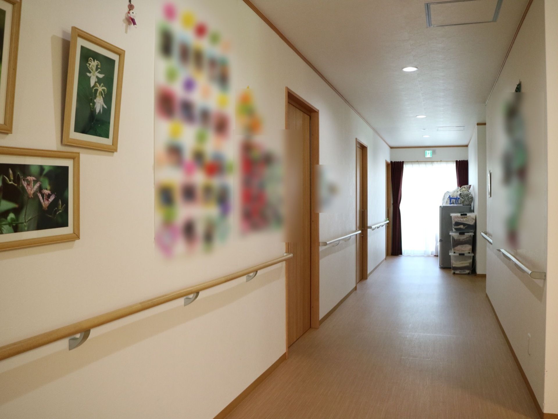 通路の壁は白色、床は茶色である。左側の壁には手すりが設置されており、上部には絵画や掲示物が飾られている。