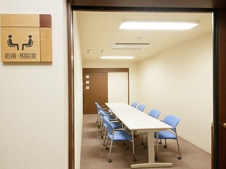 ブルーの椅子が8脚セットされた長いテーブルが置かれた部屋。壁にはなにも飾られていないシンプルなデザイン。