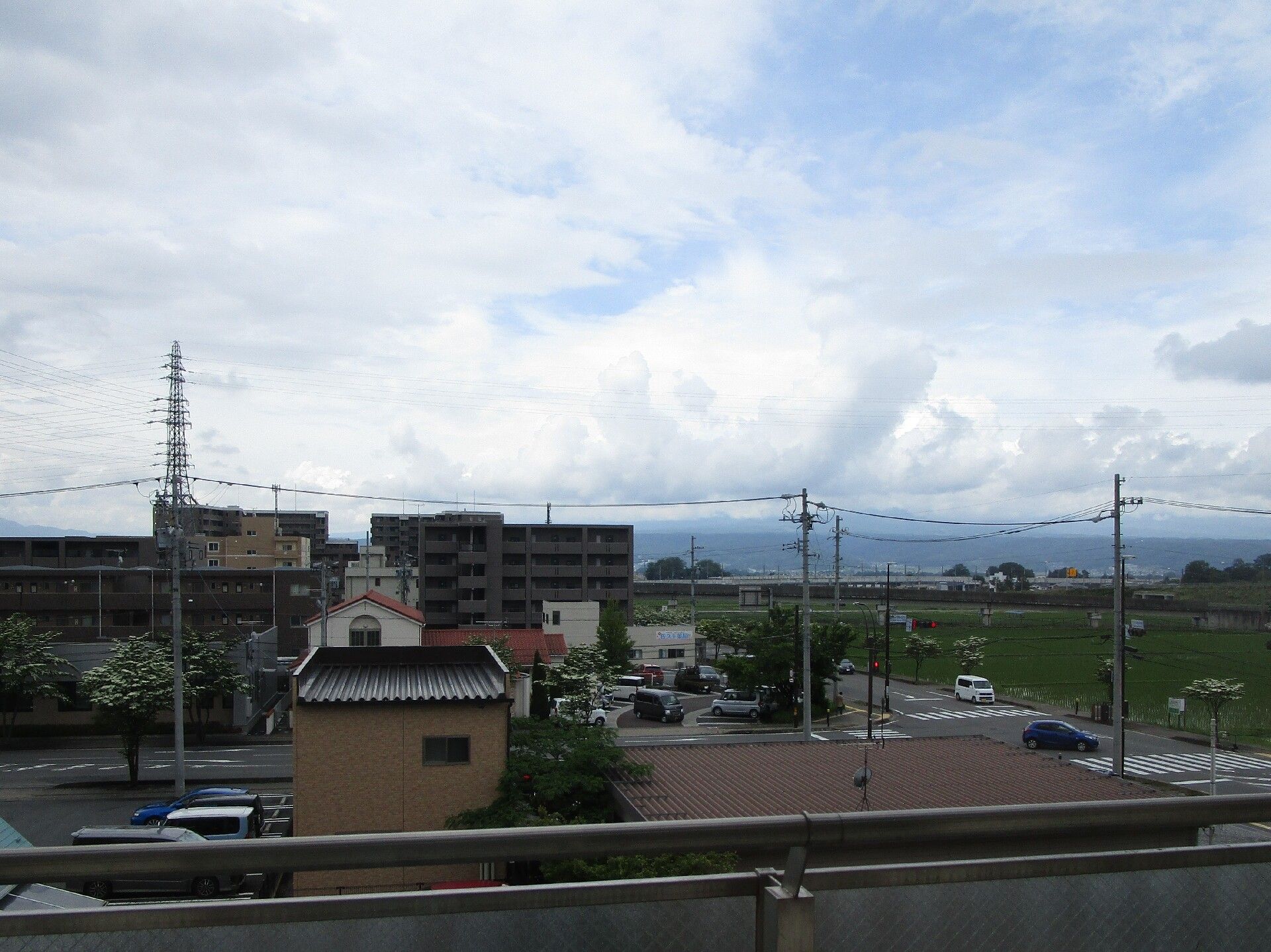 雲に覆われた空の下にはマンションのような大きなビルなど建物も多くあるが、右側には草原のような場所が広がっているなど自然も残っている。
