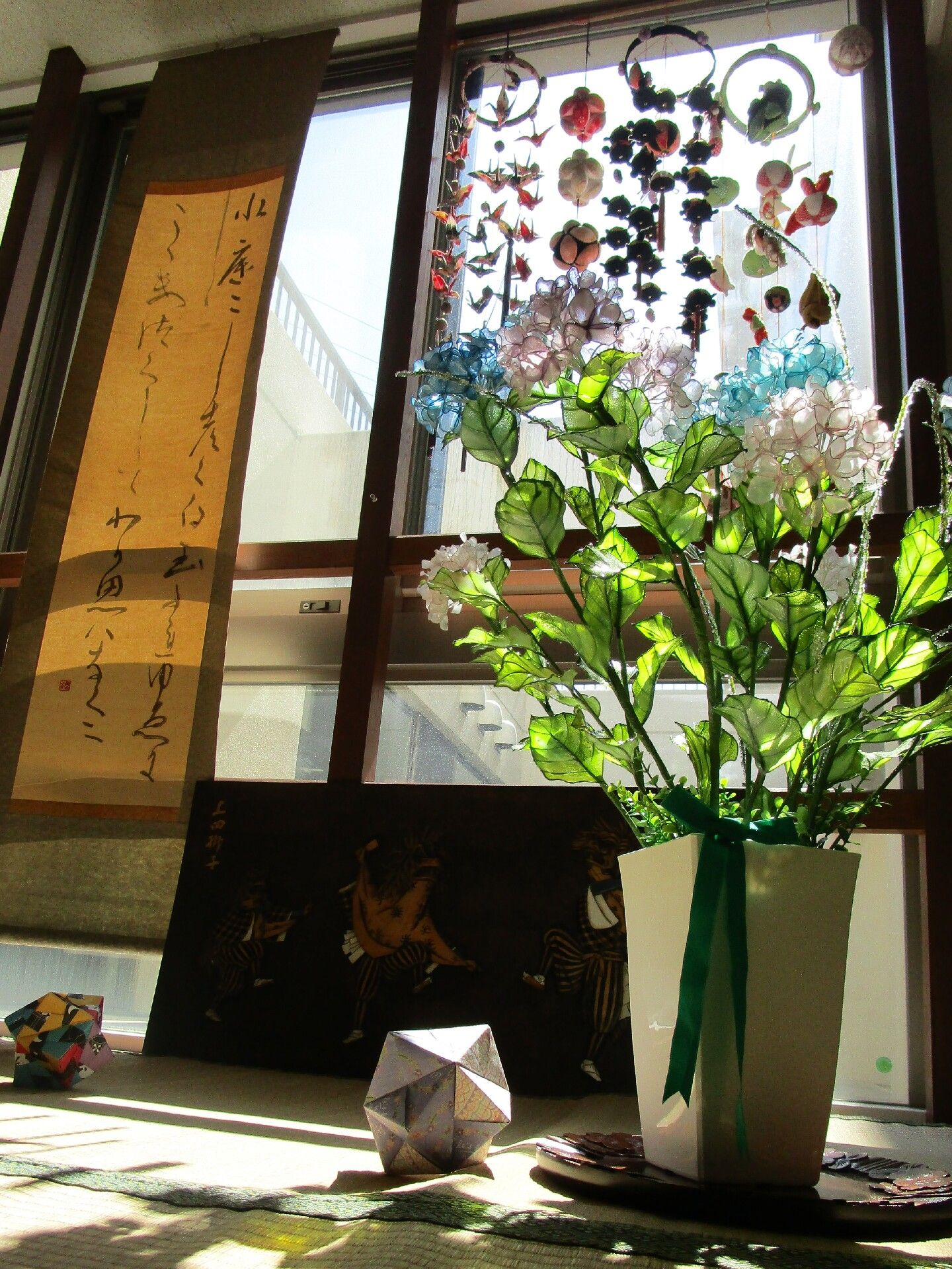 花が飾られた花瓶があり、その後ろにはドリームキャッチャーのような飾りが複数飾られていて、小さな掛け軸もかけられている。