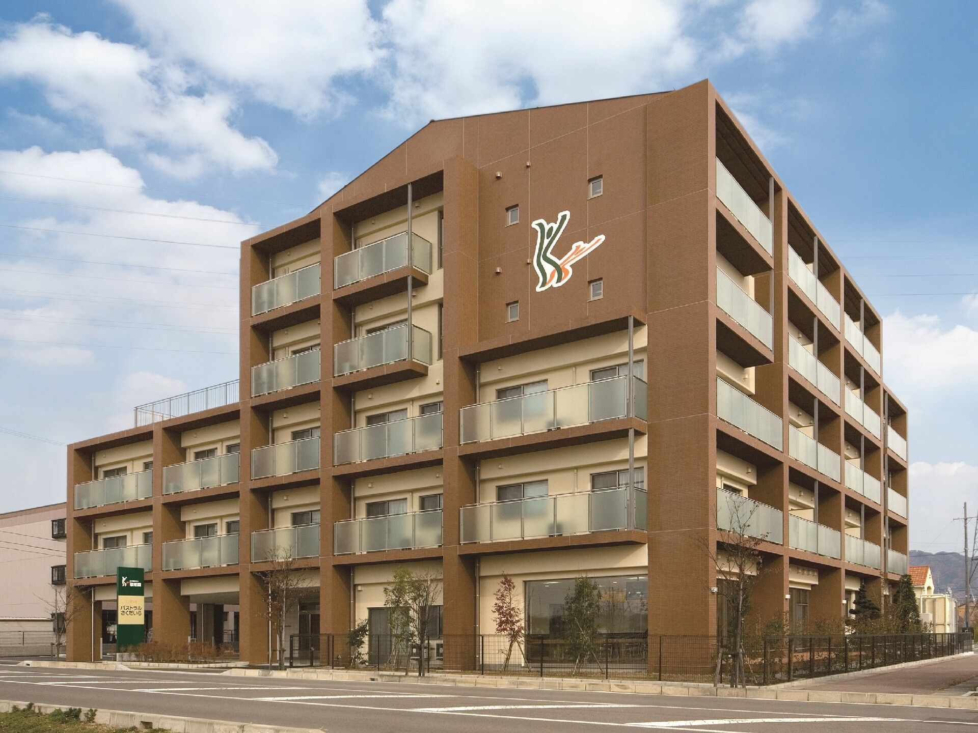 5階建てのブラウン系の建物は一部3階建てで道路に面していて、どっしりとした構え。各フロアにベランダが付き、建物周辺には木が植えられている。