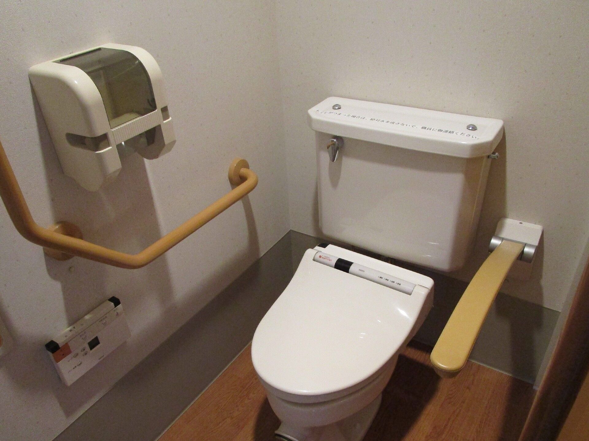 片方の壁には温水便座の操作パネルや手すり、トイレットペーパーホルダーが付き、反対側の壁には可動式の手すりが付いている。
