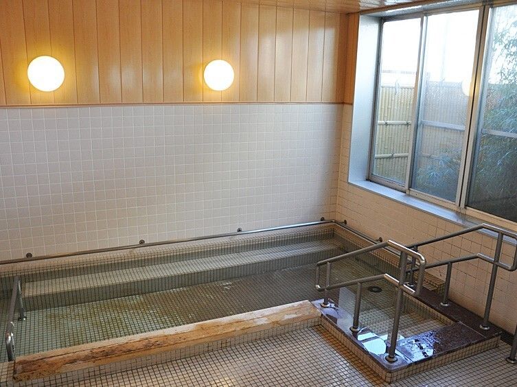 和風庭園を眺めながら入浴できる大浴場。大きな浴槽には手すり付きの階段が設置され、フロアや壁はタイル張り。照明は暖色系で温かい雰囲気。