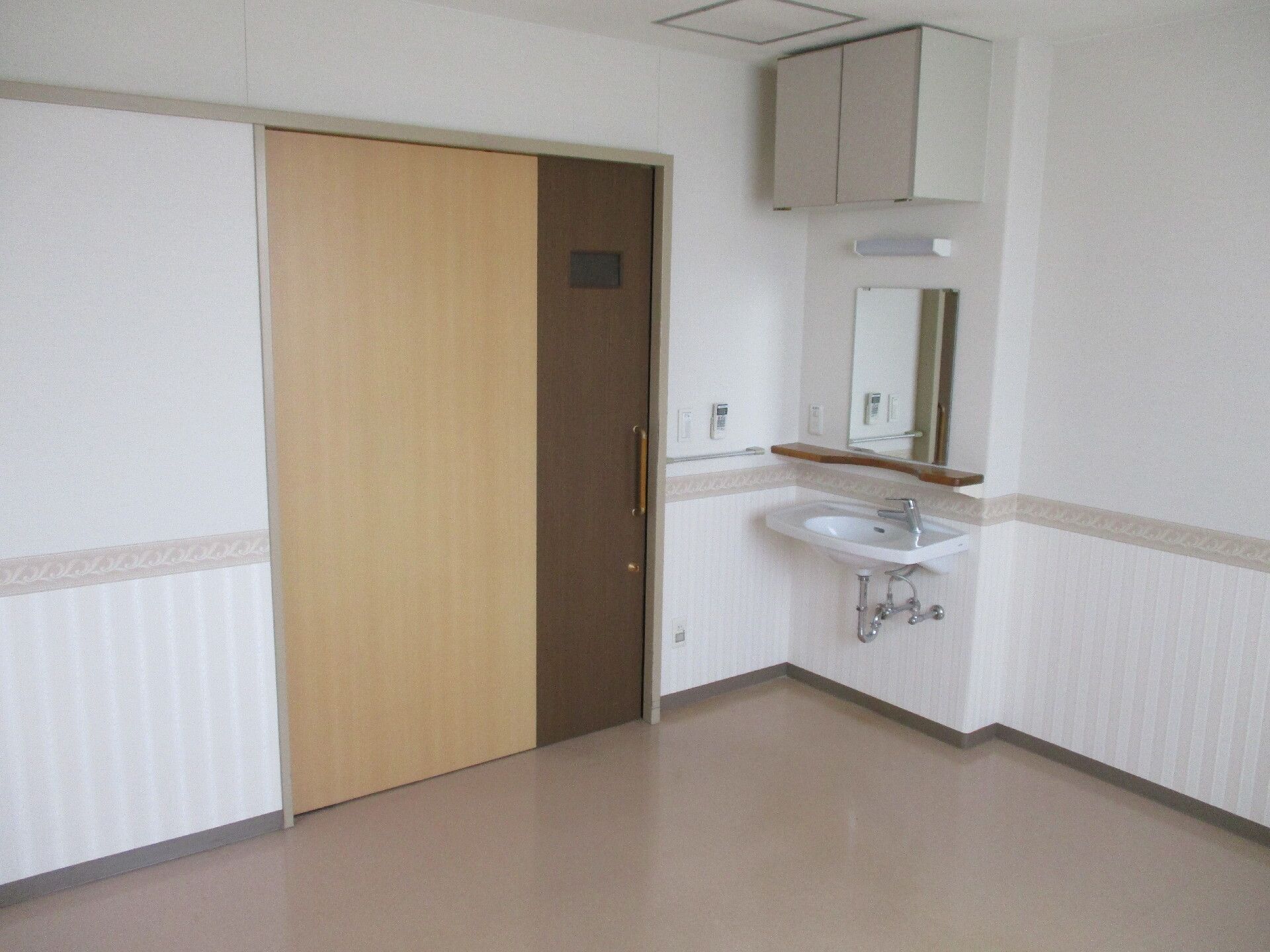 スライド式の大きなドアが付いた居室。居室には家具や家電はなく、車いす対応の洗面所のみついている。洗面所の上には収納スペースもある。