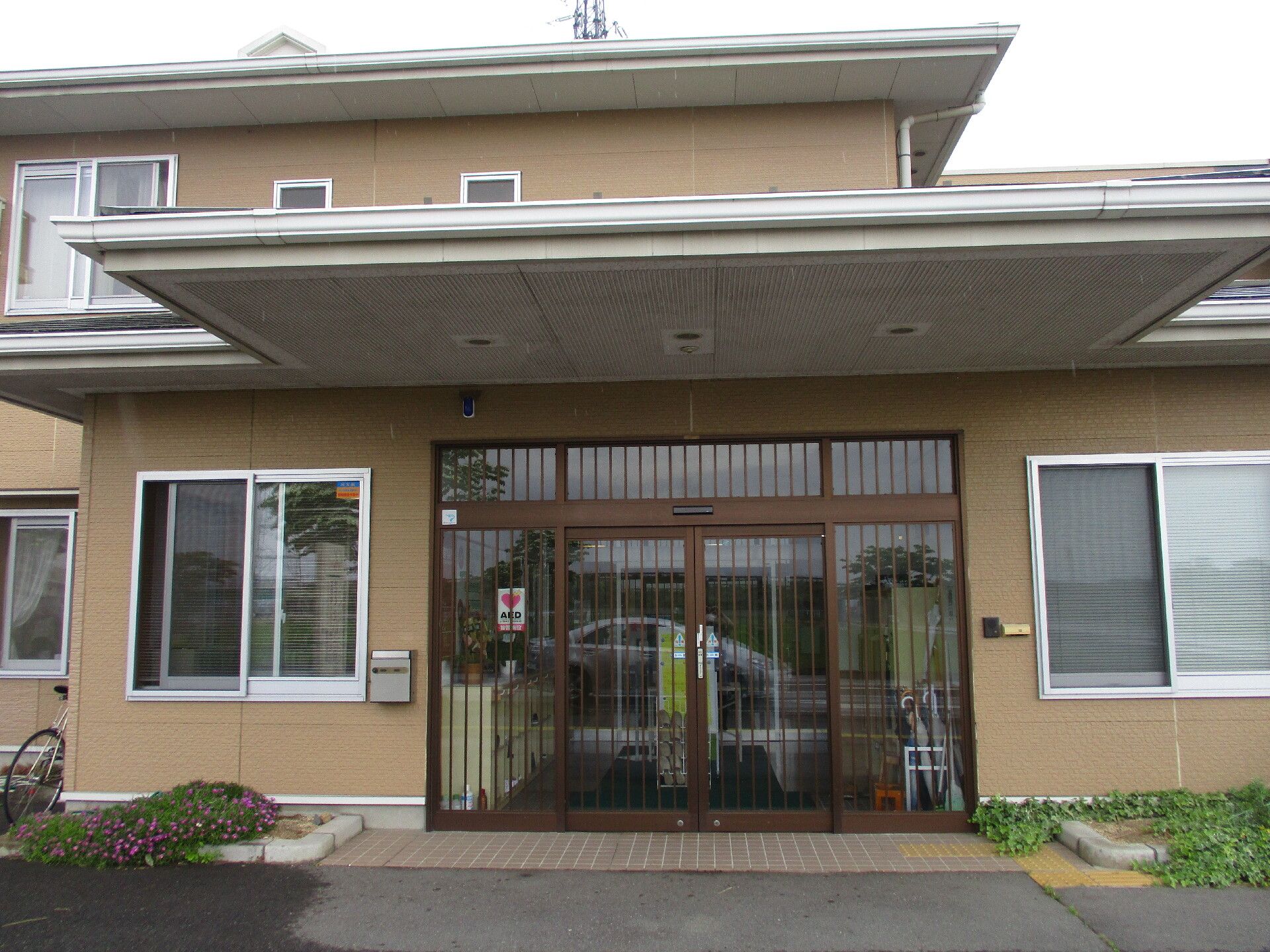 一般の住宅のような2階建ての建物。玄関前には車寄せが付き、玄関にはＡＥＤのステッカーが貼られ、玄関の内部には傘立てなどがある。