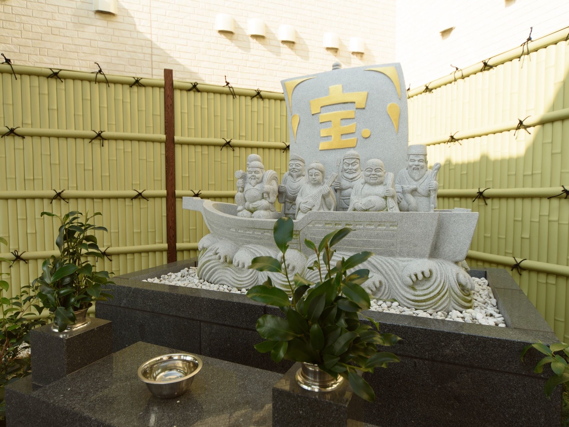 玄関すぐそばにある、宝船と七福神をかたどったエクステリア。台座は黒い御影石製で、白い玉砂利に囲まれて本体が立っている。