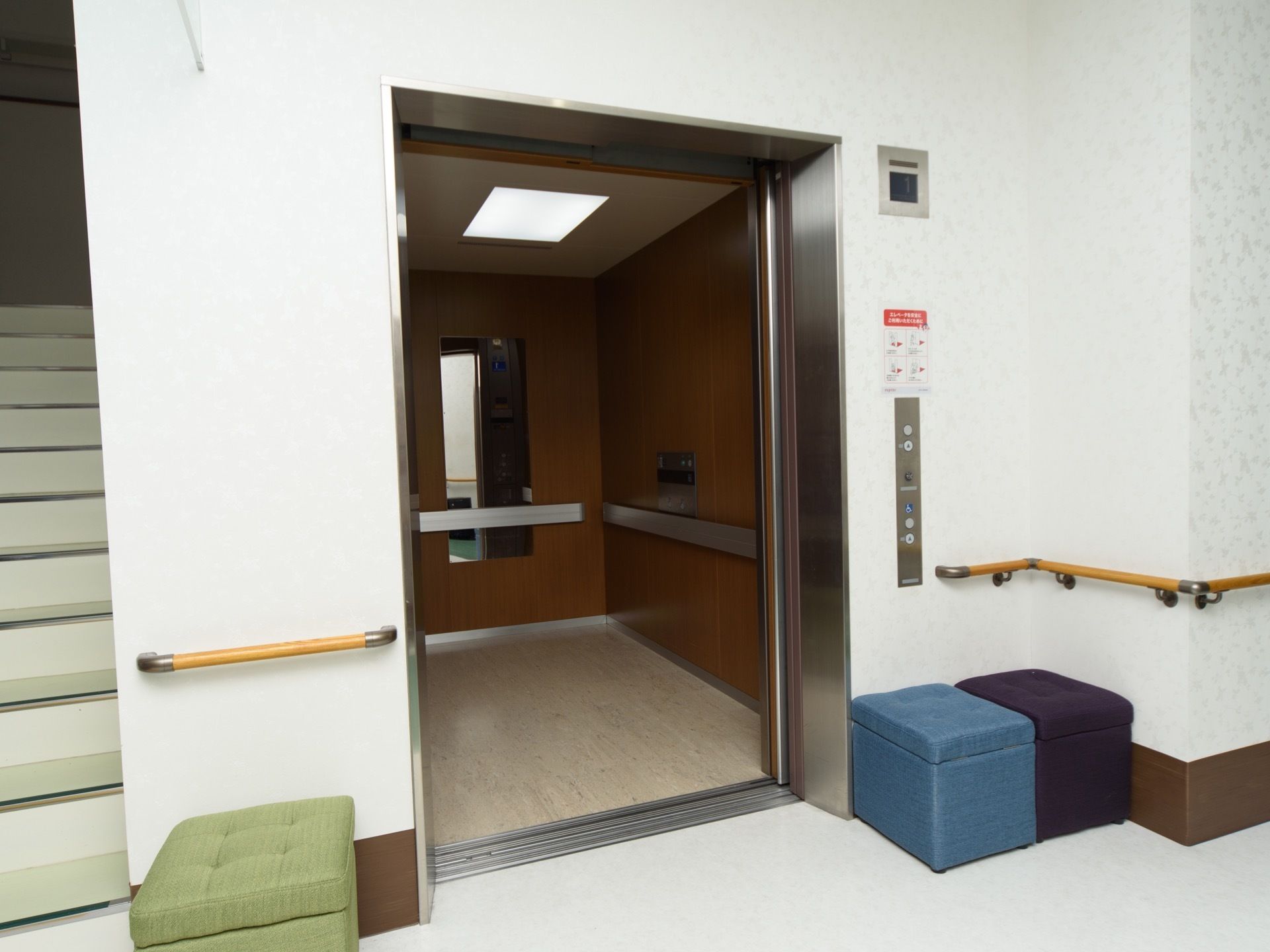 １階にあるエレベーターの乗降口。すぐ横に階段があり、ドアの手前には座って待つための箱型ソファが置かれている。