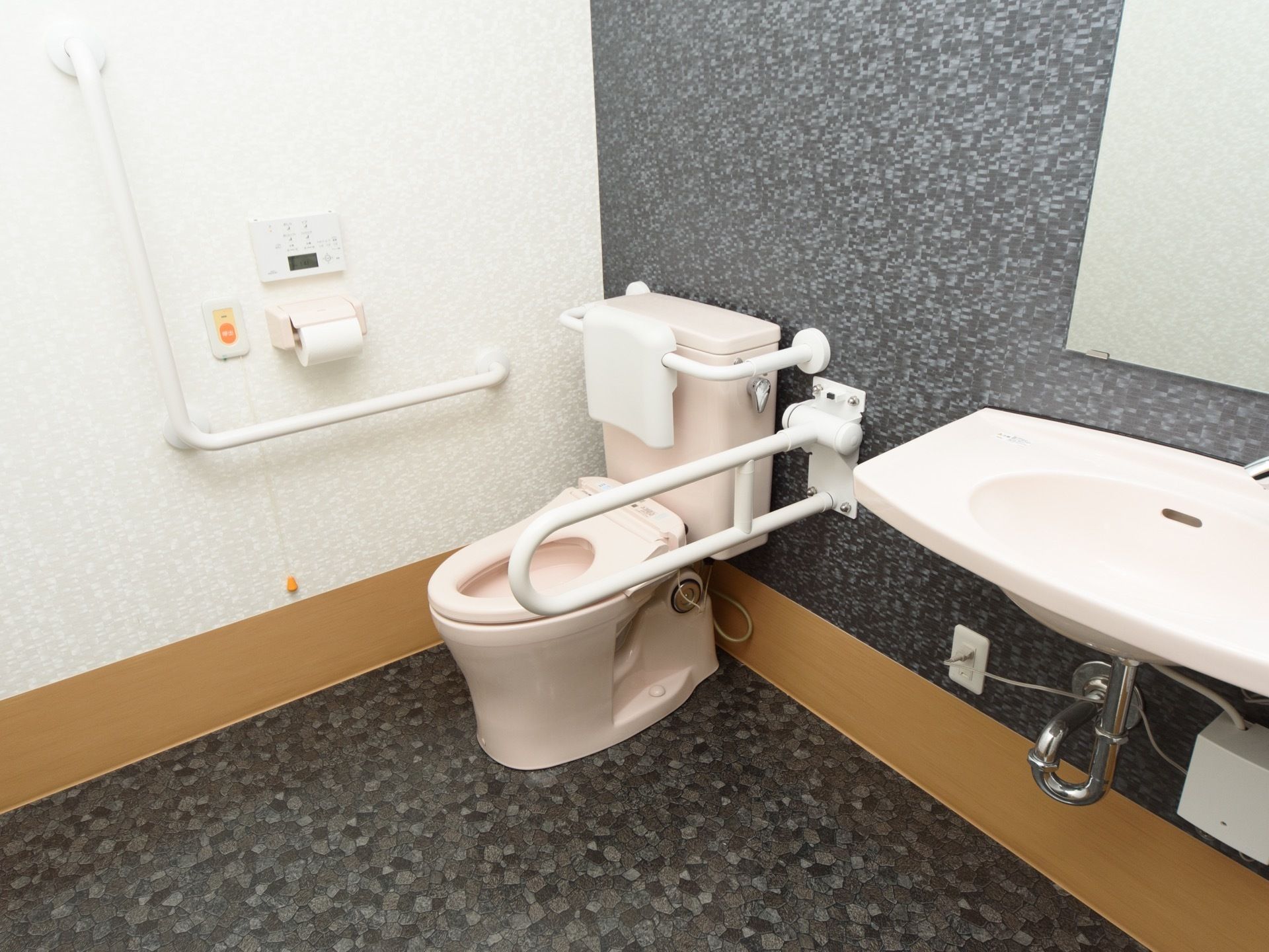 洗面台を備えた個室共用トイレの室内。広いスペースと折りたたみ型の手すりにより、車椅子対応のタイプとなっている。