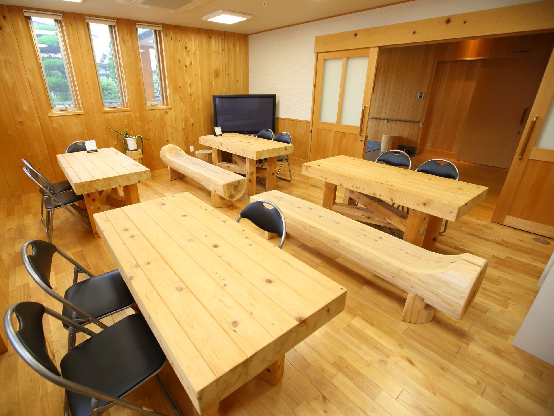 地域交流室は木の温もりが感じられる空間になっている。木材で作ったテーブルやベンチが用意されている。壁際に大型テレビが設置されている。