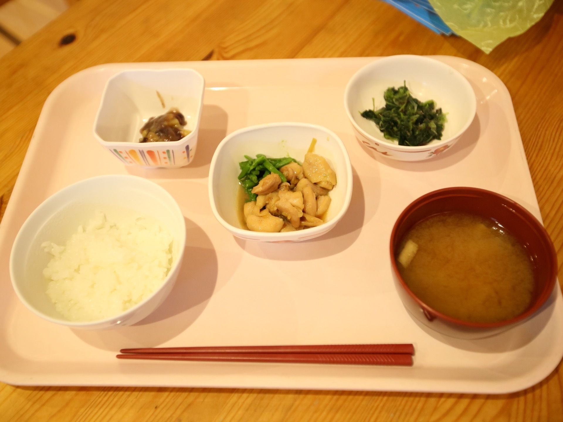テーブルの上に置かれた白いトレイには、ご飯とみそ汁、３種類のおかず入った小鉢が並べられている。箸が用意されている。