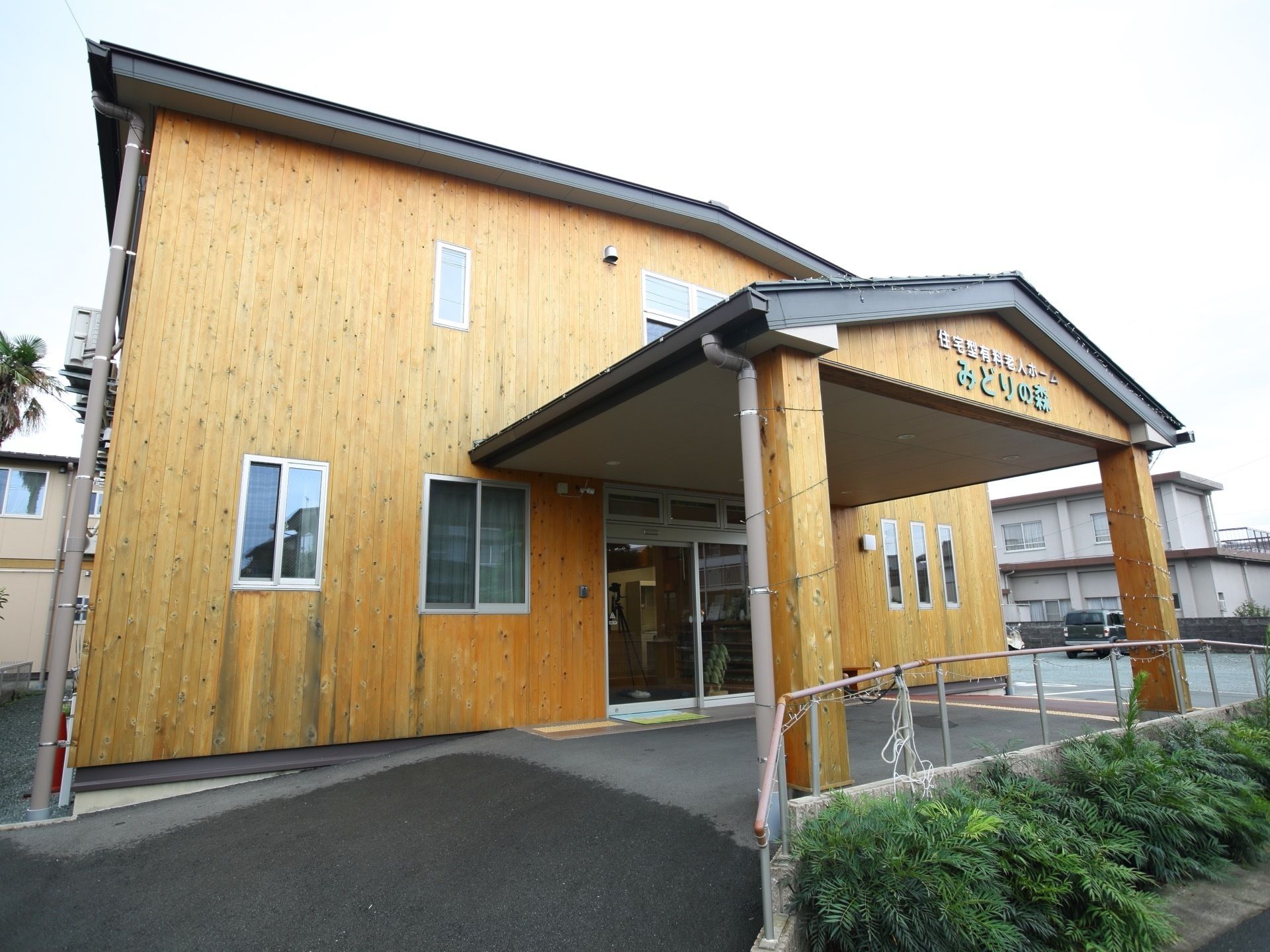 エントランスには、車寄せが設けられており、木製の大きな屋根が設置されている。向かって右奥に駐車場がある。