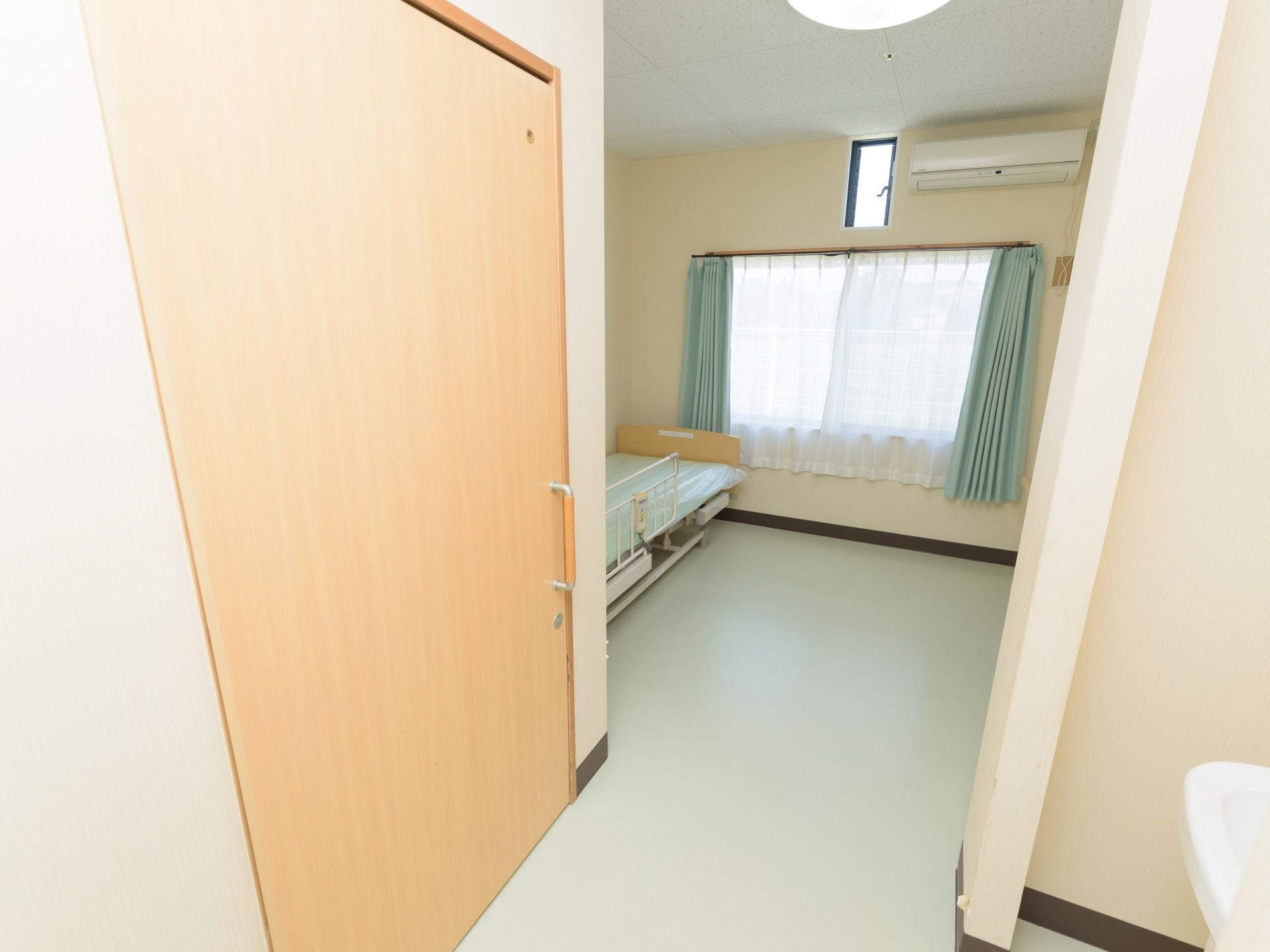 ご入居前の居室の壁には、窓やエアコン、換気窓が設けられている。フローリングには、介護用ベッドがある。