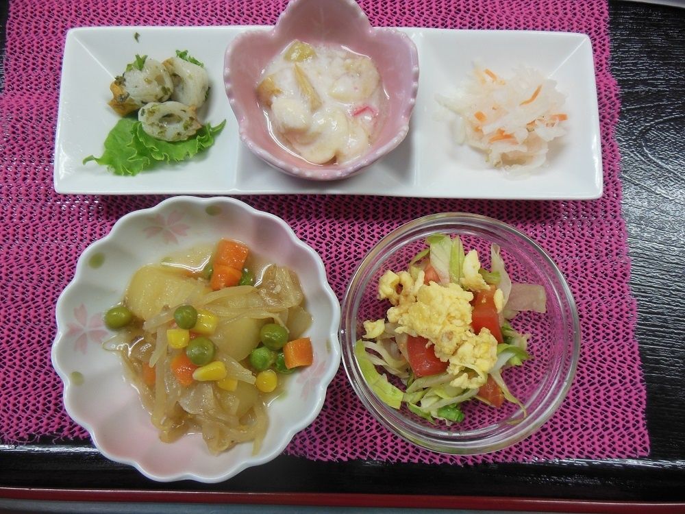 肉じゃがやサラダ、吸い物などが並べられたピンクのランチョンマット。