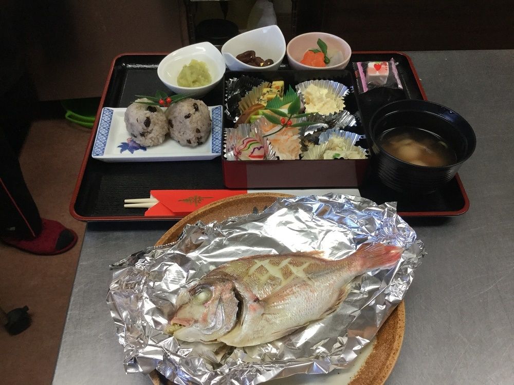 尾頭付きのタイの酒蒸しに赤飯やきょらんのあえ物、吸い物などが並んだ御馳走。