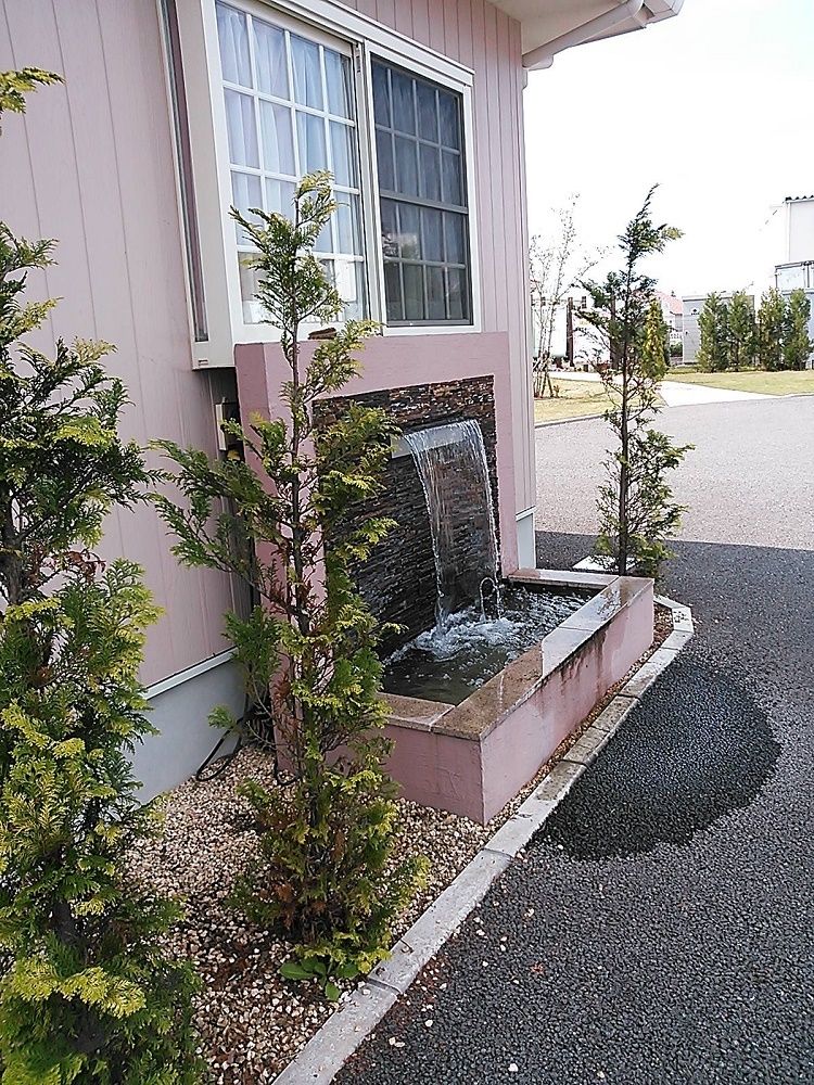 屋外の窓の下にさりげなく噴水が設置されていて、周辺には木が植えられている。