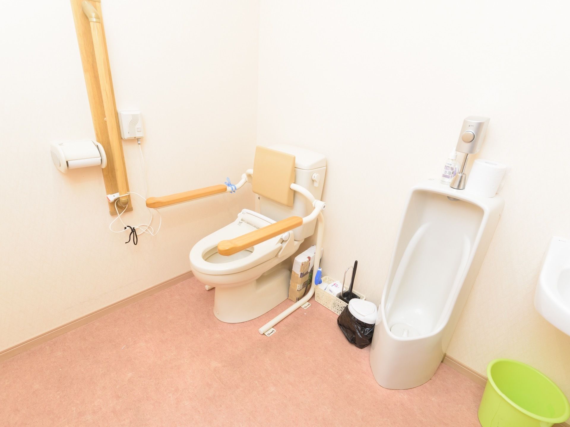 男性用の小便器と洋式便座が並んで設置されたトイレがある。洋式便座の横と近くの壁には手すりが設置されている。