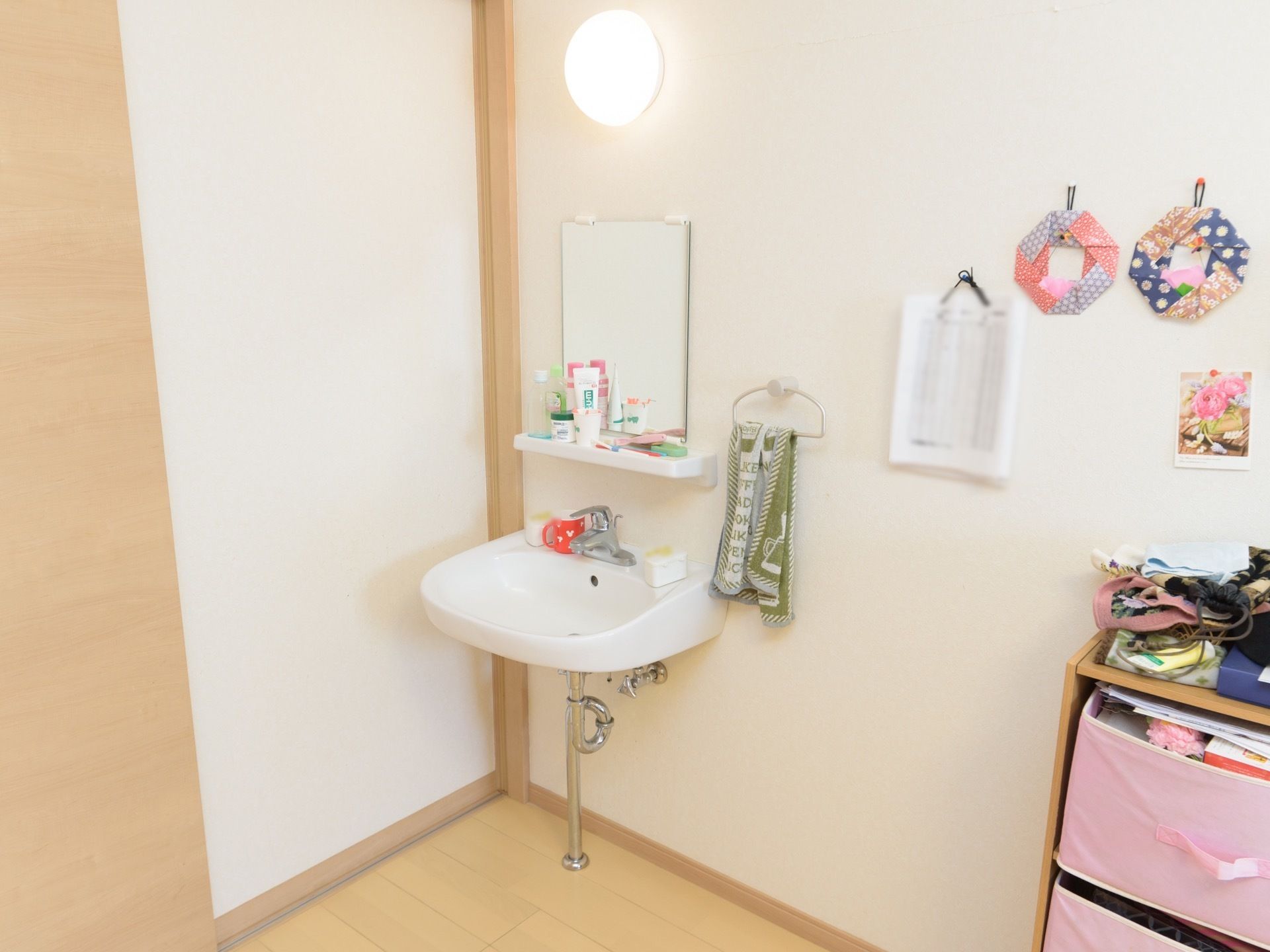 部屋の扉を入るとすぐに洗面台が設置されている。照明や鏡もあり、鏡の下は棚になっていて、コップや洗面道具が置けるようになっている。