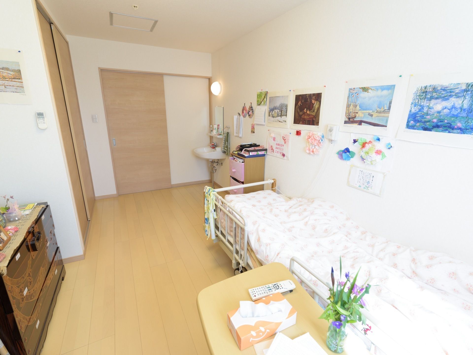 フローリングの部屋に、電動ベッドが置かれている。サイドテーブルがついていて花瓶に花が活けられている。