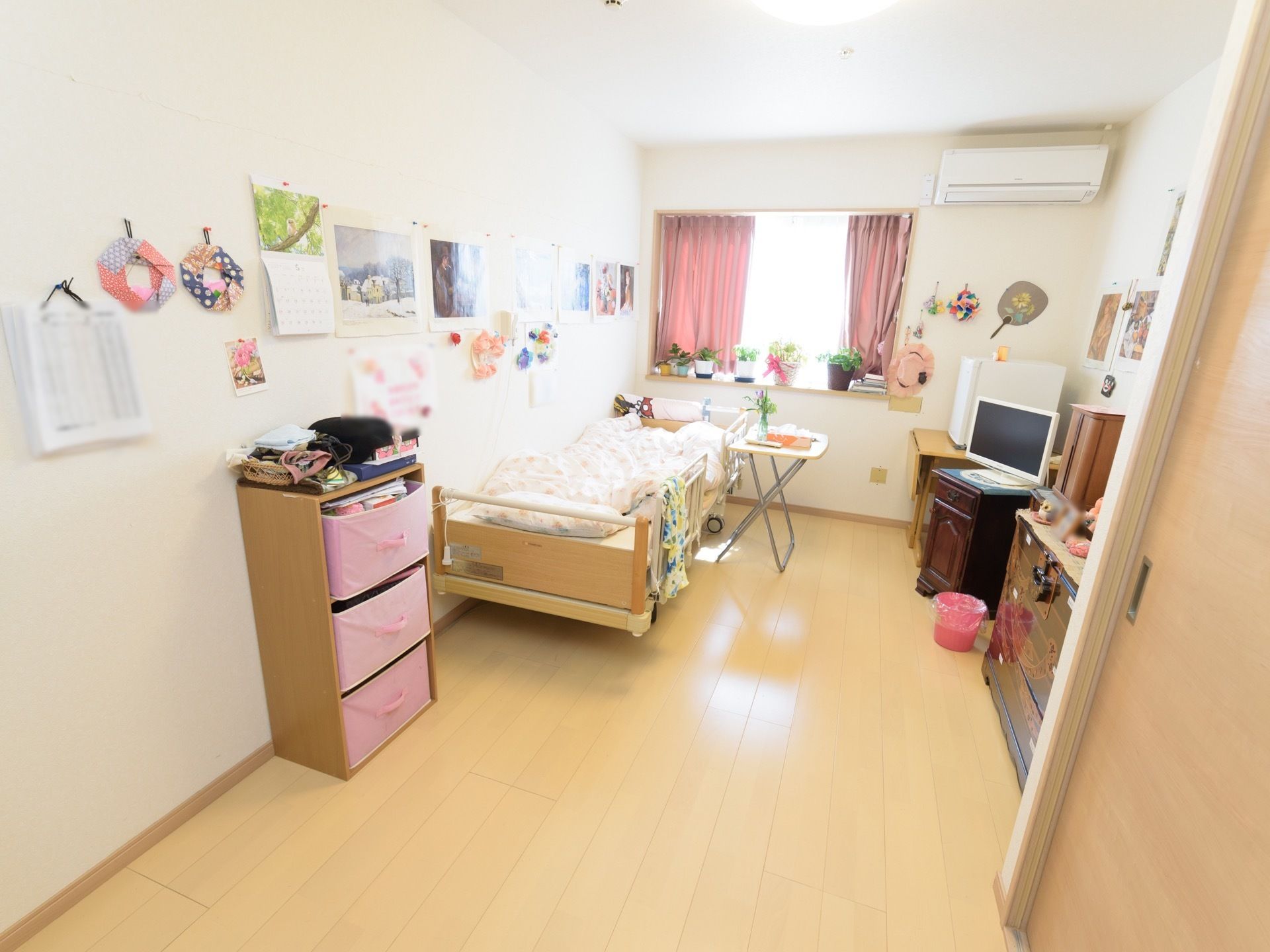 電動ベッドと３段チェスト、タンス、テレビ台などが置かれた部屋がある。窓際には鉢植えが飾られ、良く陽が当たっている。