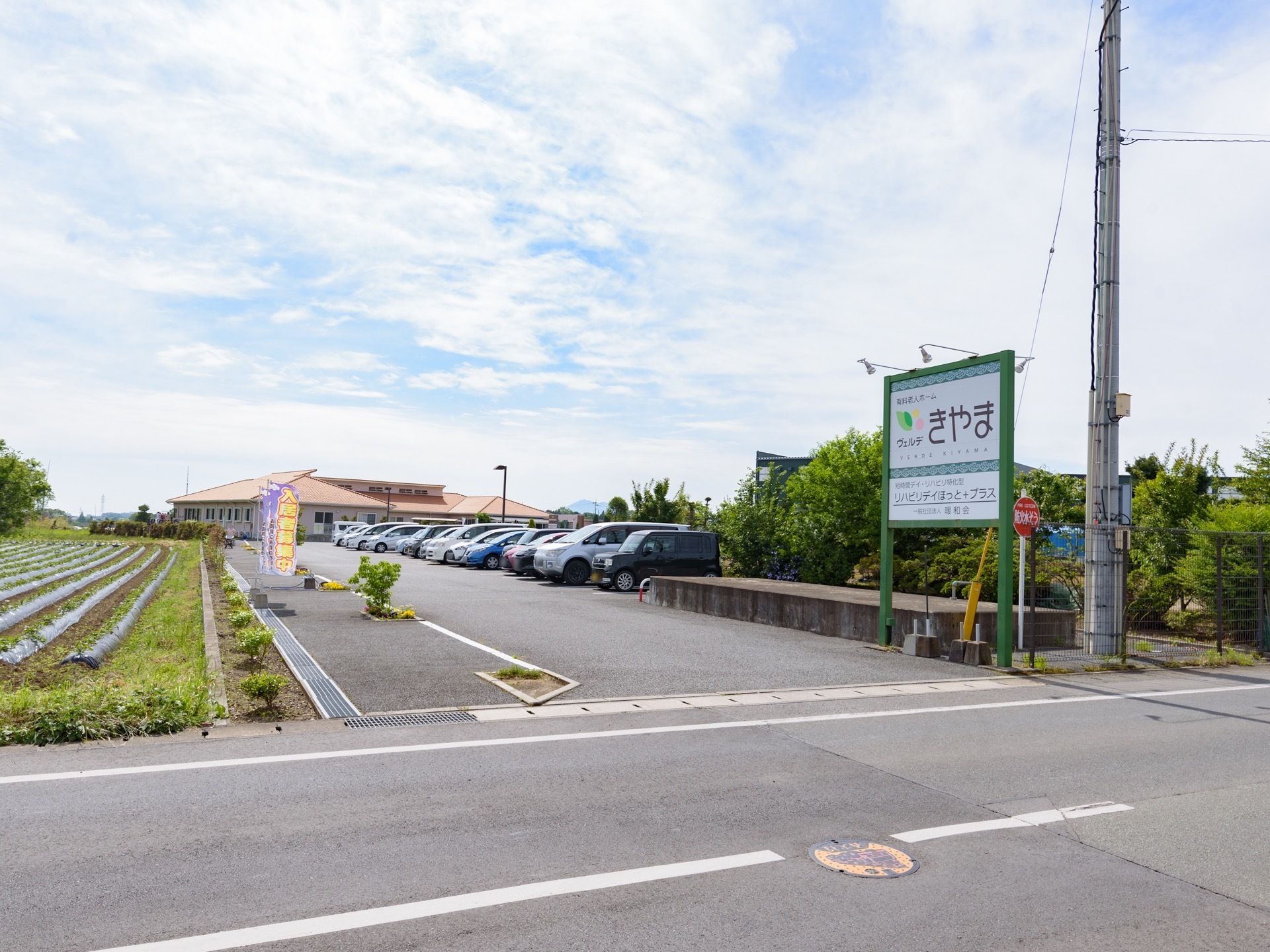 車道から広い通路が建物まで伸びている。道路から建物までが駐車場になっていて、15台以上の車が並んで停められている。