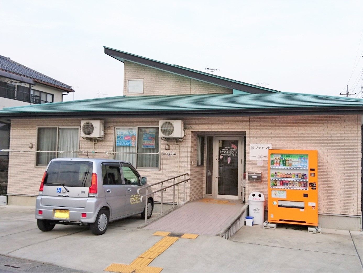 緑の屋根と駐車場スペースがある小さな一軒家風の建物。優しい色合いの建物の写真