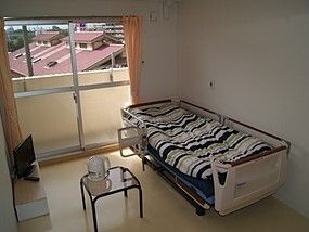 寝具付きのベッドが置かれた部屋にはテーブルやテレビもあり、カーテンが付いたおおきな窓がある。