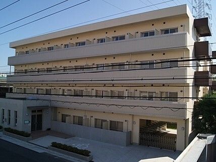 各フロアにベランダが付いている4階建てのベージュの建物の前には駐車場がある。