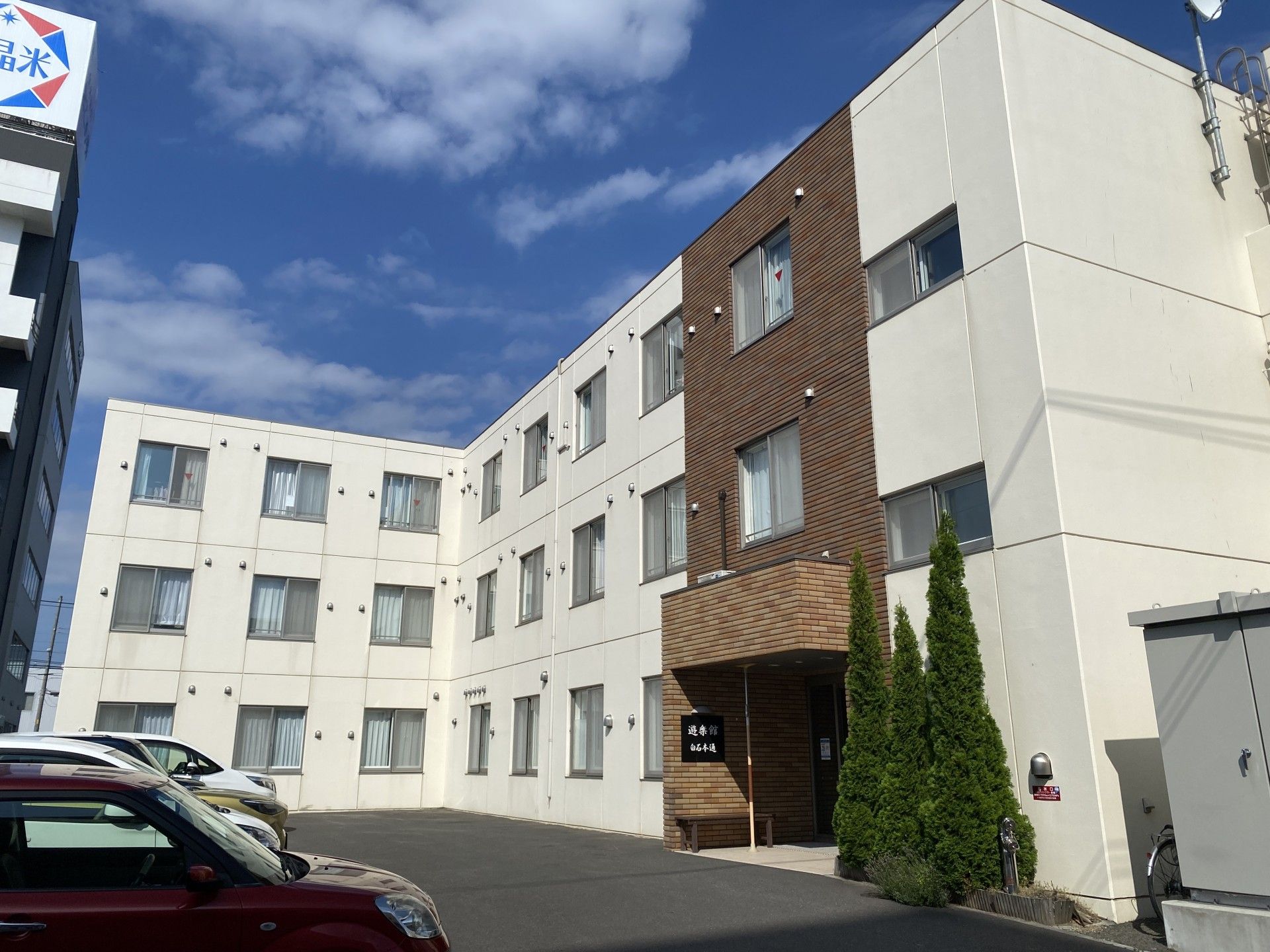 3階建ての建物はエル字型で玄関の周りには草木が植えられ、広い駐車場がある。