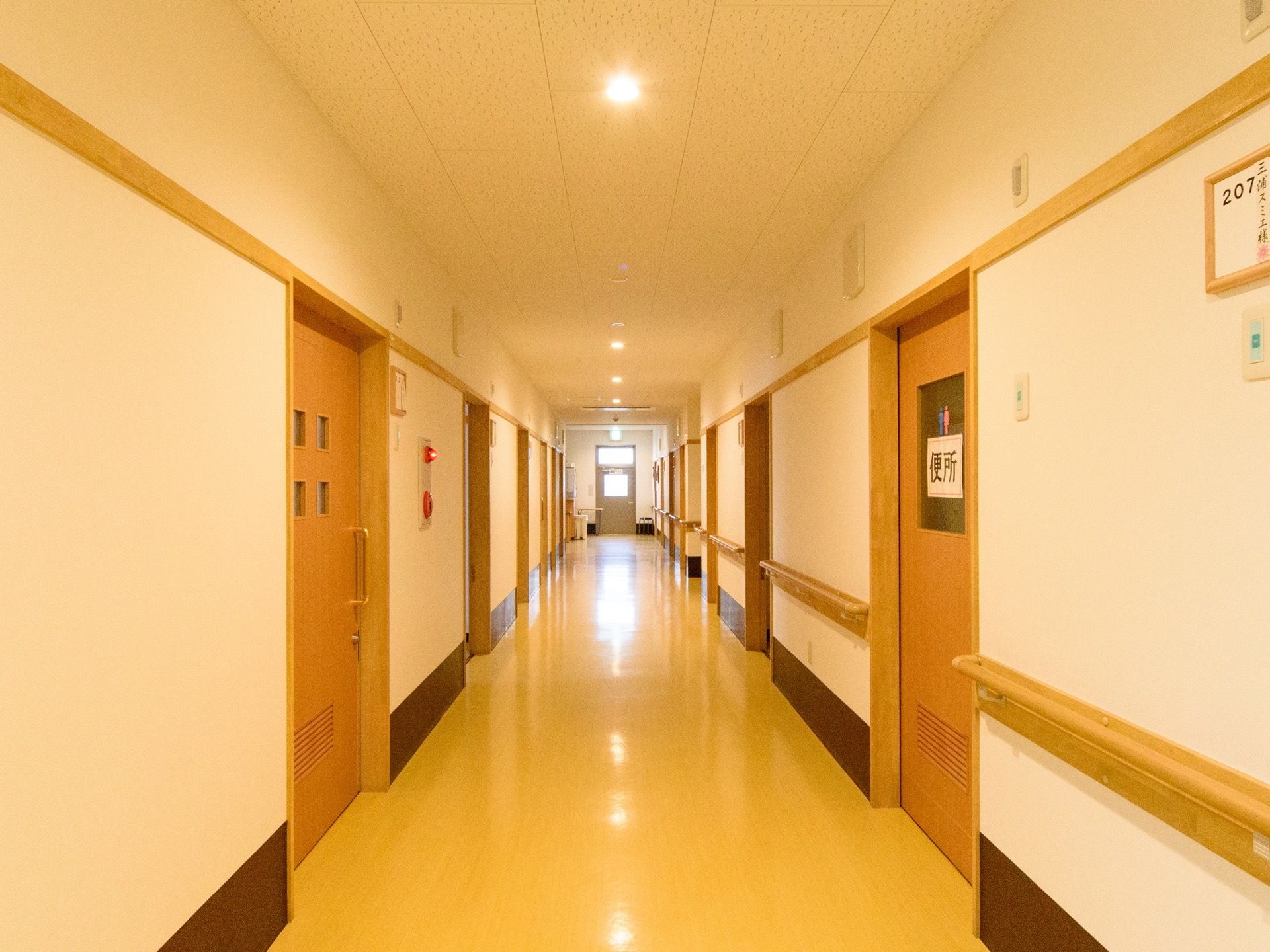 まっすぐで見通しのよい廊下である。共用トイレの入口扉のガラス部分に性別のマークと文字が表示されている。