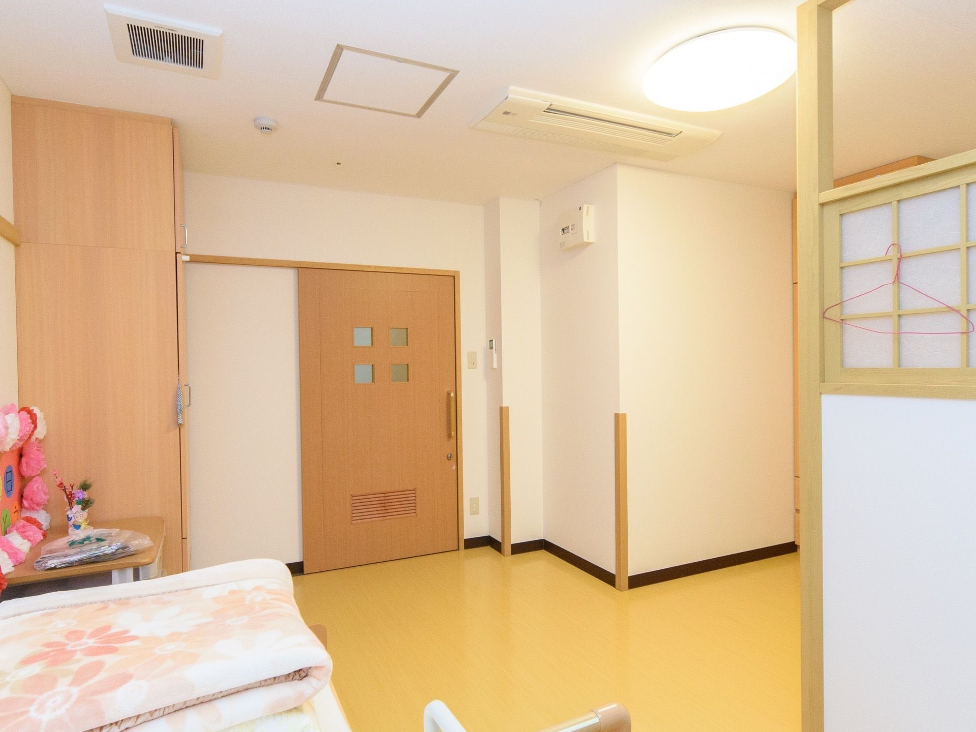 居室に入ってすぐの所に、天井までの高さがある収納スペースが設置されている。ベッドの近くに和風の感じがするパーティションがある。
