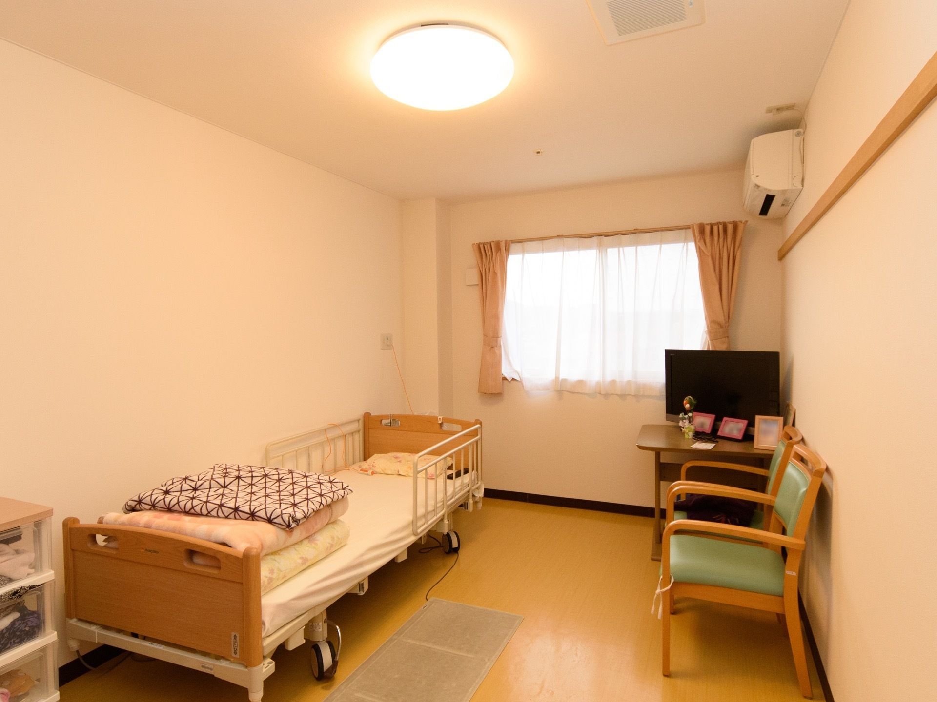 居室に腰高の窓があり、レースのカーテンが閉められている。窓の右側の壁の上の方にエアコンが設置されている。