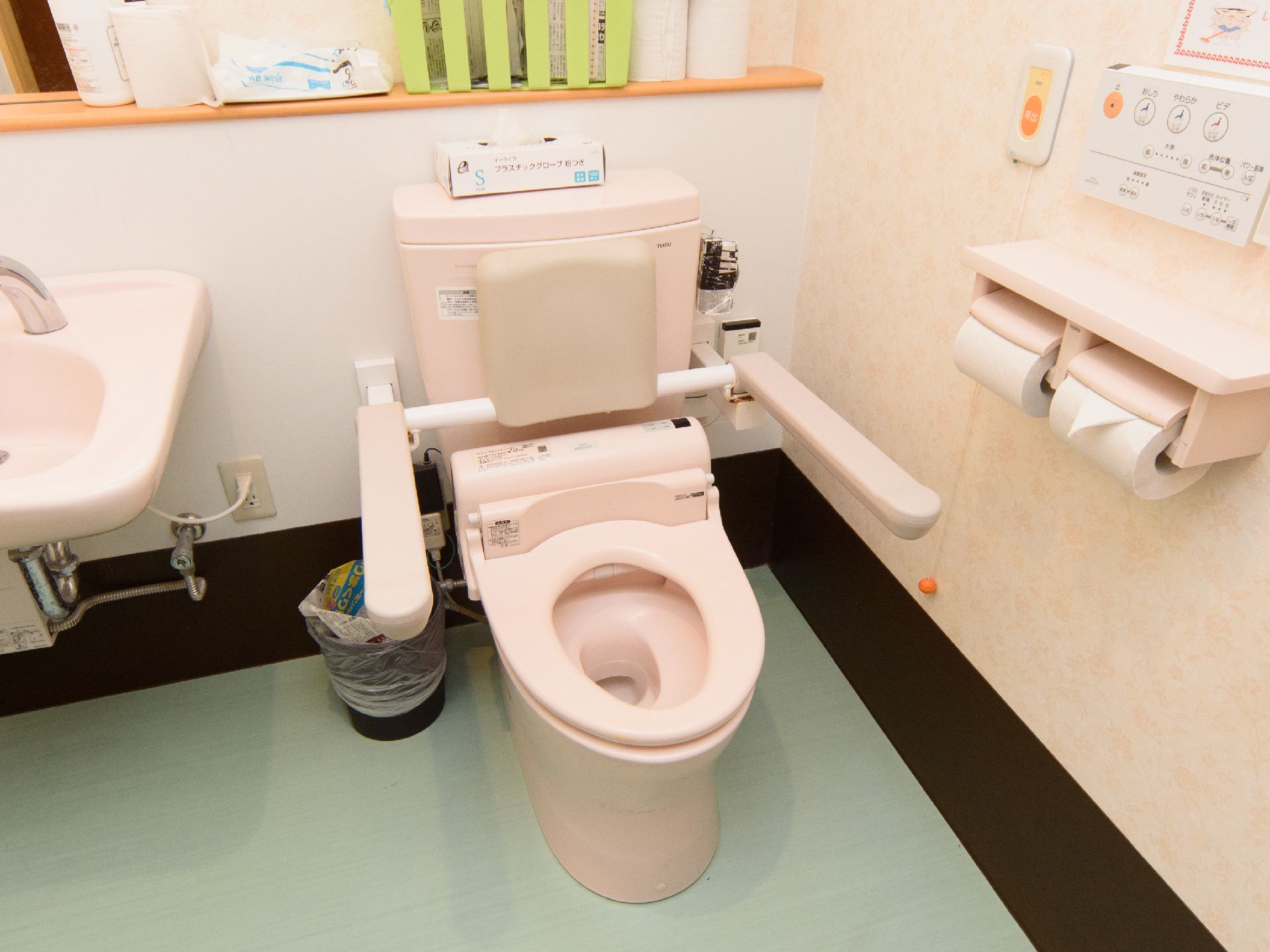 便器の両側に手すりが付いており、すぐ横に洗面台が備わったトイレ
