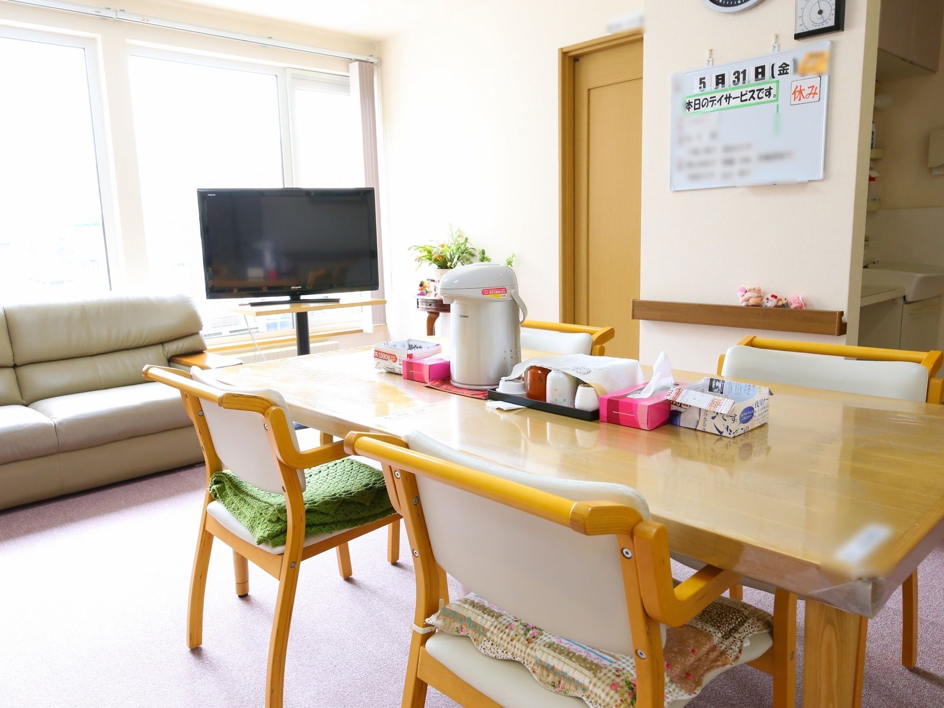 明るい色調の木のテーブルに椅子が４つある食堂。テーブルの上にはポットと茶器が置かれている。大きな窓のある壁際にはソファとテレビがある。