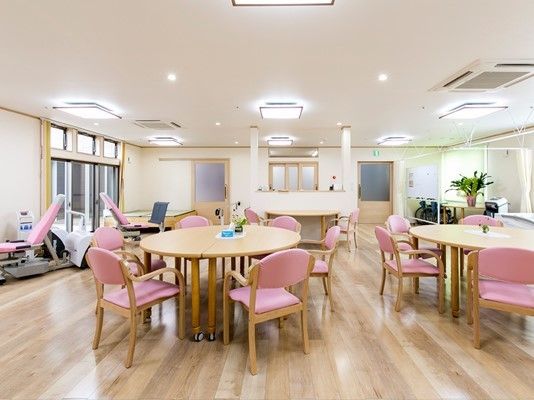 大きな窓が付いた共有スペース。ピンクの椅子がセットされたダイニングテーブルが複数置かれている。