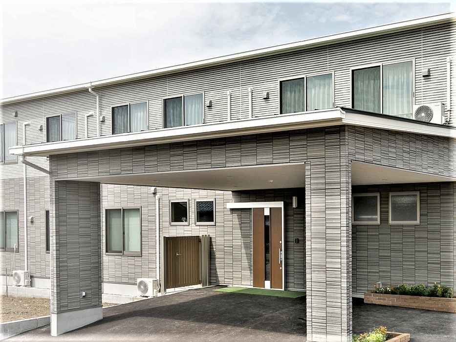 ブラウン系でまとめられたどっしりとした建物。玄関には大きな屋根が付き、花壇もある。