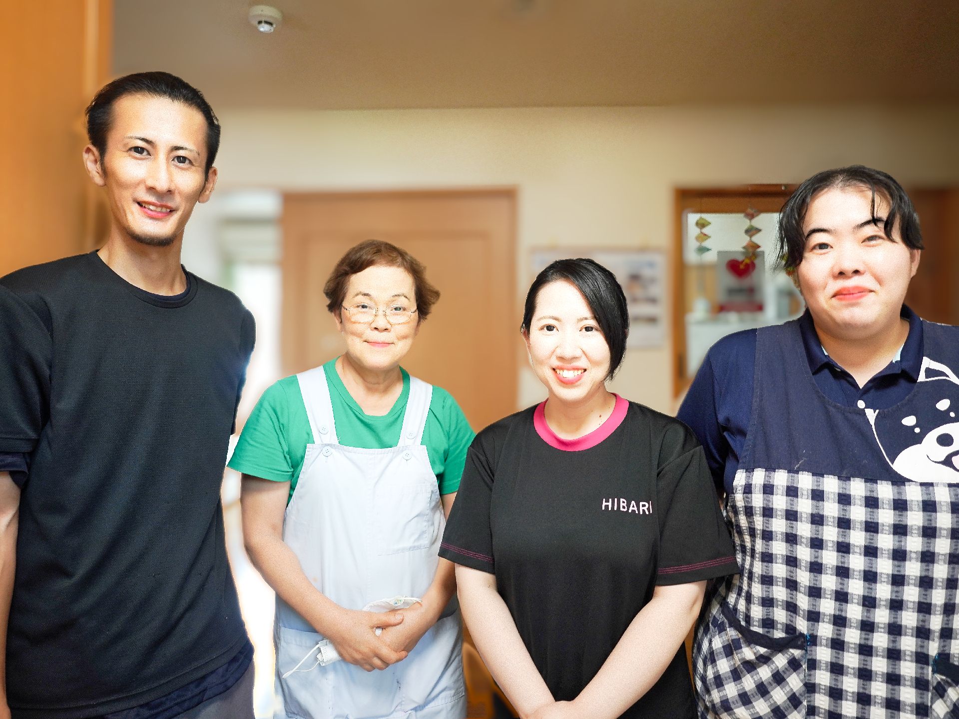 福祉車両から下りようとしている眼鏡をかけた高齢男性の手伝いをしているエプロンを付けたスタッフ。